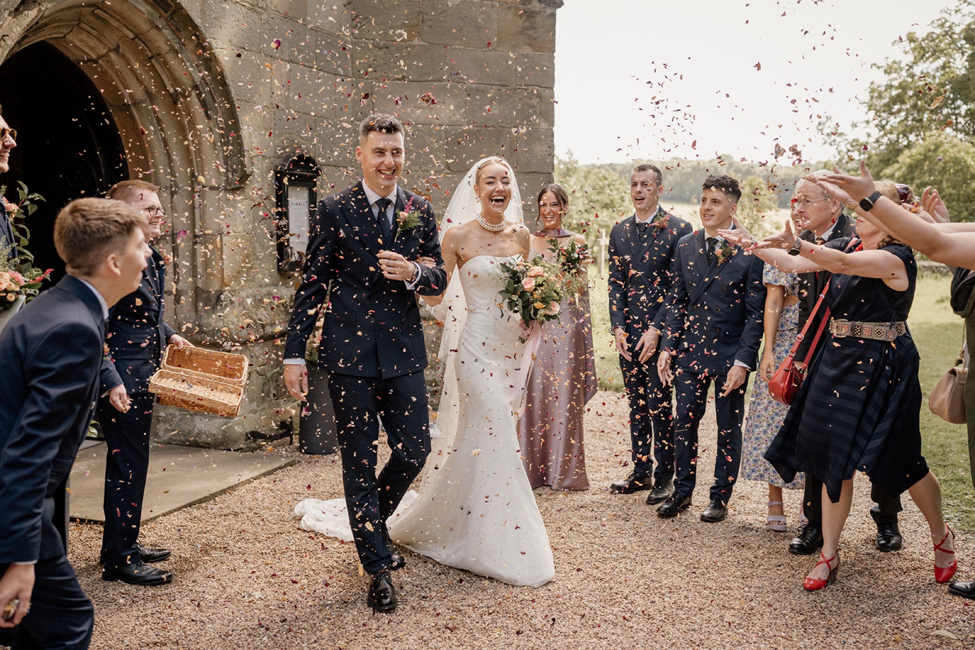 Newlyweds walking through a confetti shower from a stone arch